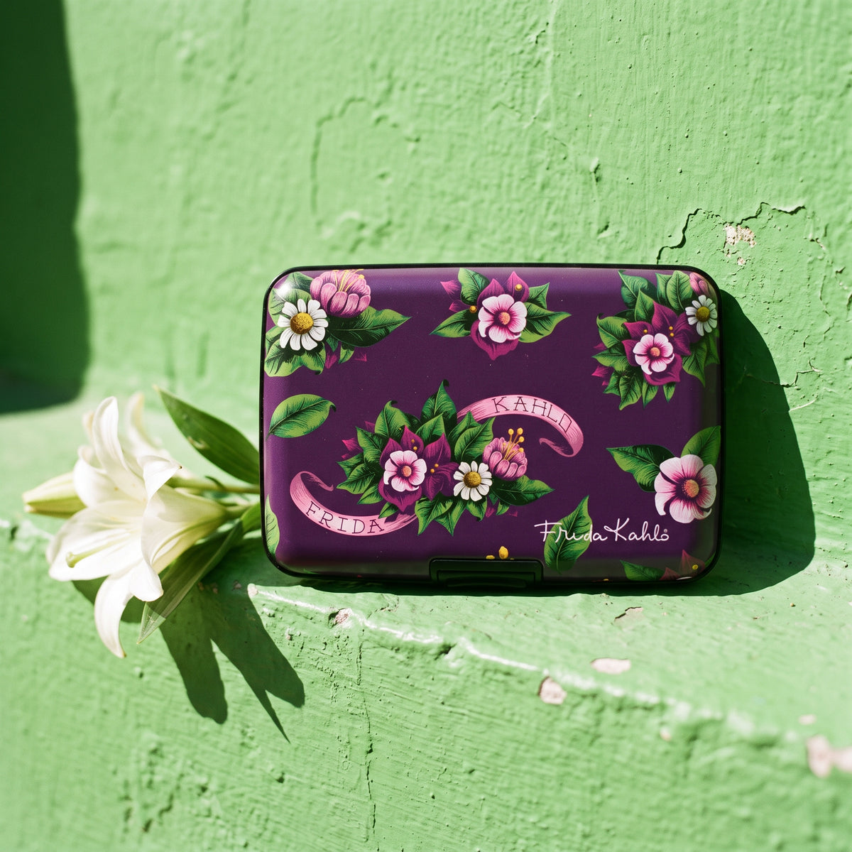 Frida Kahlo Purple Floral armored RFID wallet on a green wall with a white lily