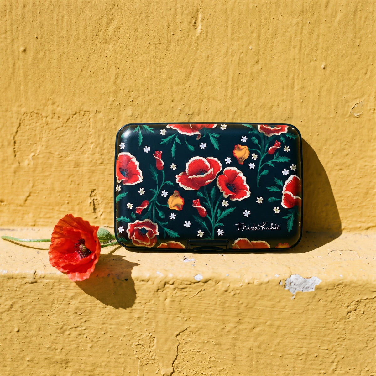 Frida Kahlo Poppies armored RFID wallet on a yellow wall with a red poppy