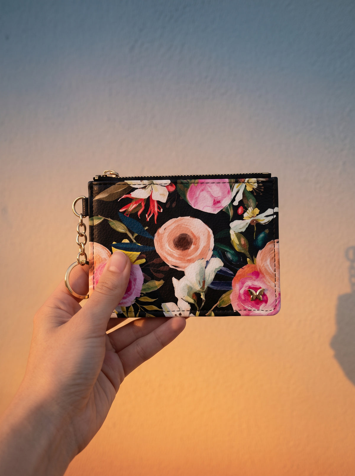 Floral on Black keychain wallet held up against a sunset-lit wall
